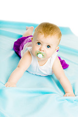 Image showing baby girl with pacifier crawling on the blue coverlet