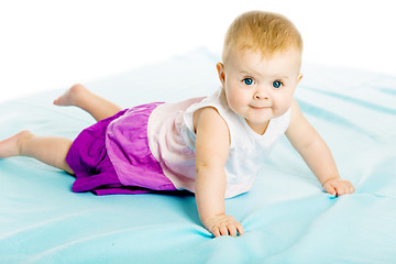 Image showing baby girl in a dress creeps on the blue coverlet