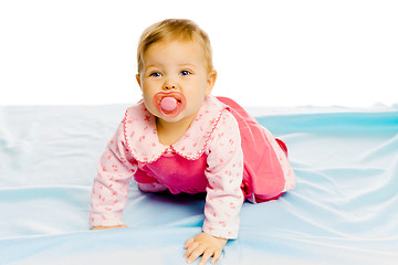 Image showing baby girl with pacifier crawling on the blue coverlet. Studio