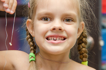 Image showing Six year old girl holding her lost tooth on a string