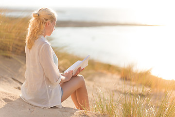 Image showing Woman enjoys reading on beautiful sandy beach.