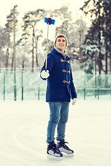 Image showing happy young man with smartphone on ice rink