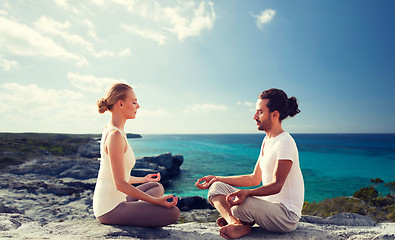 Image showing happy couple meditating in lotus pose on beach