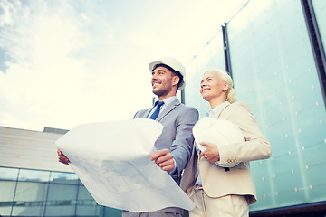 Image showing smiling businessmen with blueprint and helmets