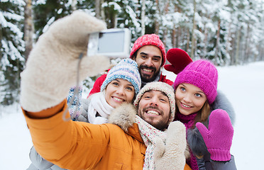 Image showing smiling friends with camera in winter forest