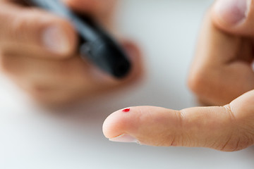 Image showing close up of male finger with blood and glucometer