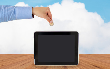 Image showing close up of hand putting coin into tablet pc