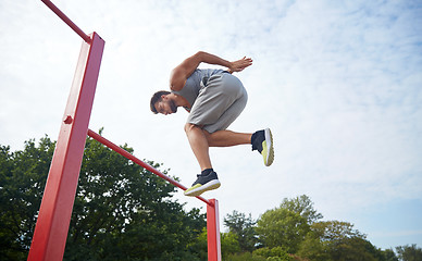 Image showing young man jumping on horizontal bar outdoors