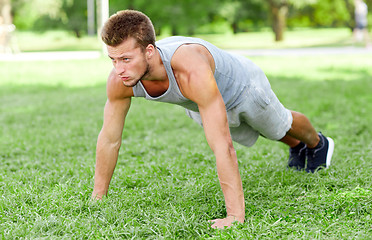 Image showing young man doing push ups on grass in summer park