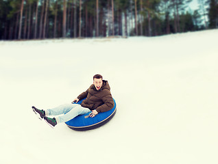 Image showing happy young man sliding down on snow tube