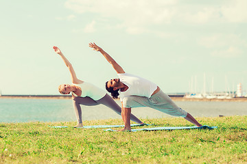 Image showing smiling couple making yoga exercises outdoors