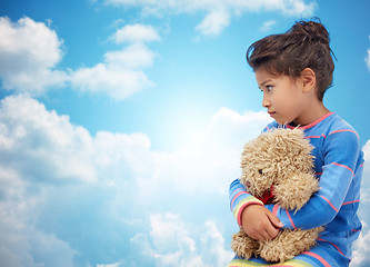 Image showing sad little girl with teddy bear toy over blue sky