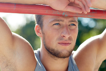 Image showing young man exercising on horizontal bar outdoors