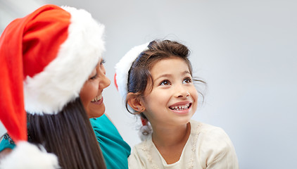 Image showing happy mother and little girl in santa hats at home