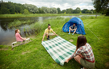 Image showing happy friends laying picnic blanket at campsite