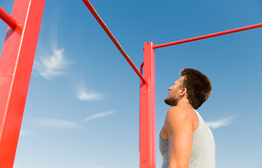 Image showing young man exercising on horizontal bar outdoors