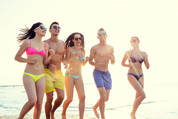 Image showing smiling friends in sunglasses running on beach