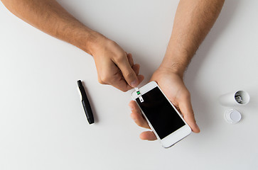 Image showing close up of man with smartphone making blood test