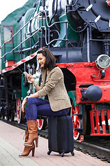 Image showing woman sitting on a trunk road and uses the phone