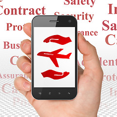 Image showing Insurance concept: Hand Holding Smartphone with Airplane And Palm on display