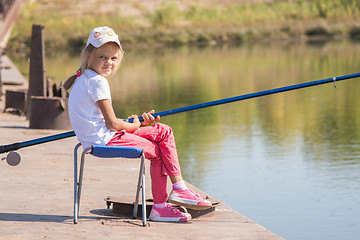 Image showing Girl fishing sitting on a chair on the bridge