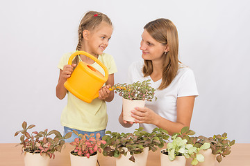 Image showing Happy mother and daughter looking at each other watering flowers