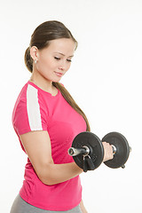 Image showing Girl athlete is looking at dumbbell in hand