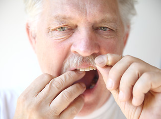 Image showing Senior man flosses teeth. 