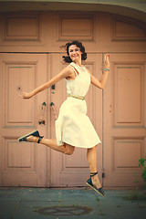 Image showing woman in a white dress smiles and jumps near the old door