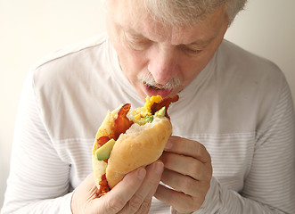 Image showing Older man eats bacon, egg and avocado sandwich 