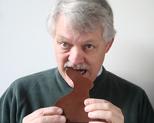 Image showing senior man bites into chocolate rabbit 