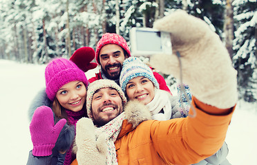 Image showing smiling friends with camera in winter forest