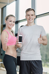 Image showing smiling young woman with personal trainer in gym