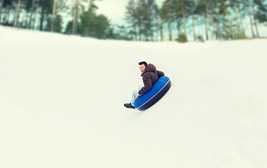 Image showing happy young man sliding down on snow tube