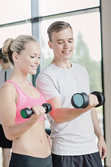 Image showing smiling young woman with personal trainer in gym