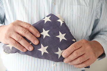 Image showing Man holds folded American flag.	