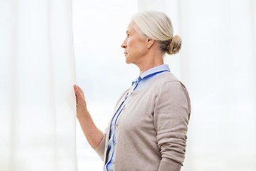 Image showing lonely senior woman looking through window at home