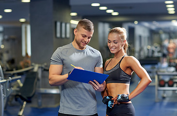 Image showing smiling young woman with personal trainer in gym