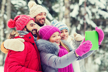 Image showing smiling friends with tablet pc in winter forest