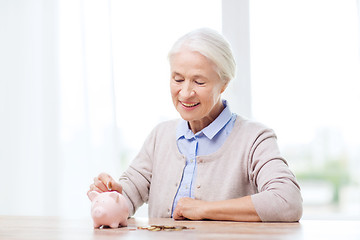 Image showing senior woman putting money to piggy bank at home