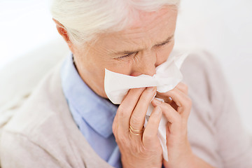 Image showing sick senior woman blowing nose to paper napkin