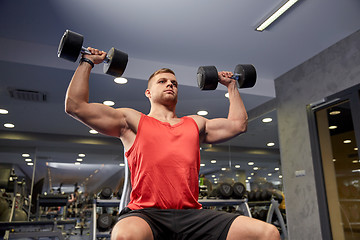 Image showing young man with dumbbells flexing muscles in gym