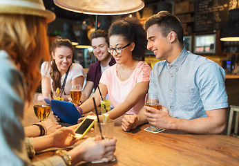 Image showing happy friends with tablet pc and drinks at bar