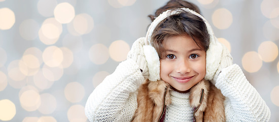 Image showing happy little girl in earmuffs over holidays lights