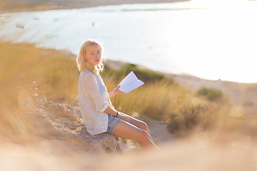 Image showing Woman enjoys reading on beautiful sandy beach.