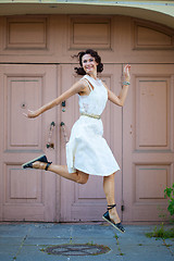 Image showing woman in a white dress smiles and jumps near the old door