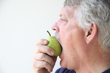 Image showing Older man bites into pear. 