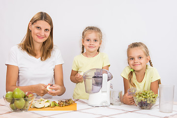 Image showing Mom and daughter sit at the table and cut fruit for juicing