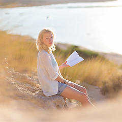 Image showing Woman enjoys reading on beautiful sandy beach.