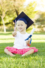 Image showing Little Girl In Grass Wearing Graduation Cap Holding Diploma With